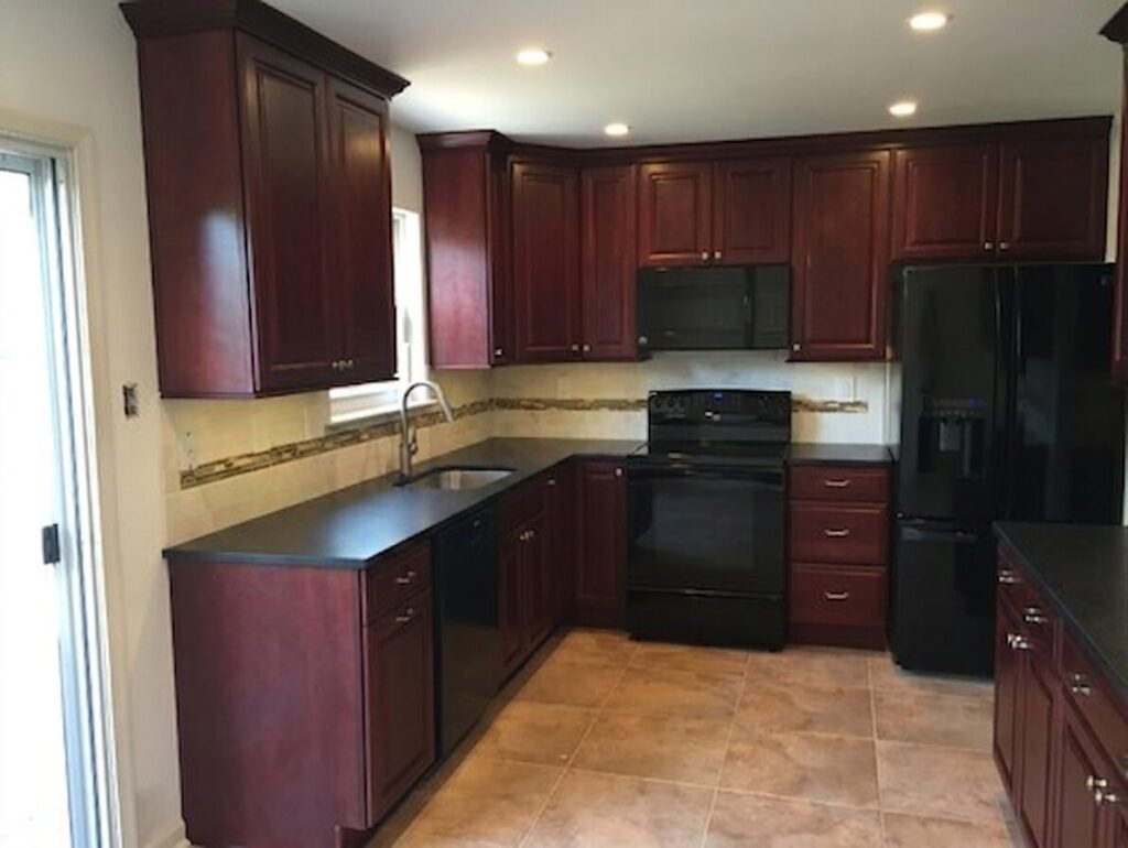 image showing kitchen with cherry wood cabinets, black countertops, tilebacksplash and tile floor