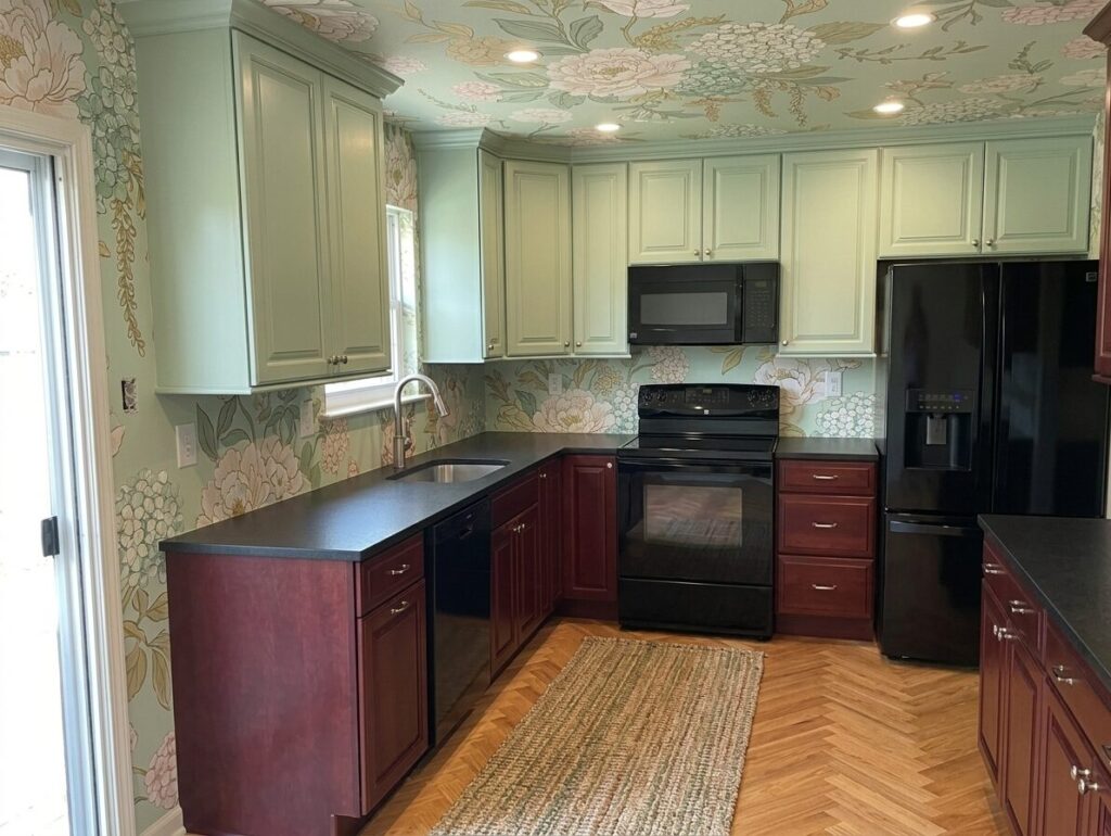 image showing kitchen with cherry wood cabinets, pastel green upper cabinets, black countertops, floral wallpaper on walls and ceilings, and black tiles